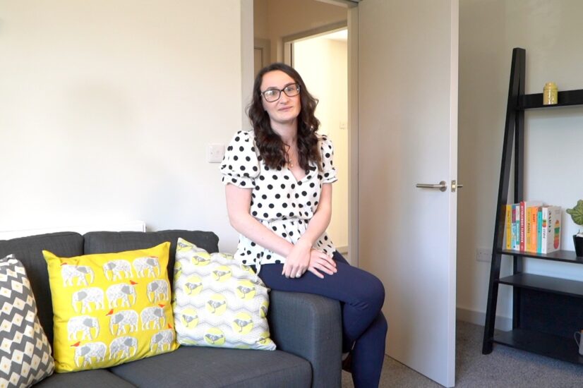 A woman sits on the arm of a grey sofa in a new property